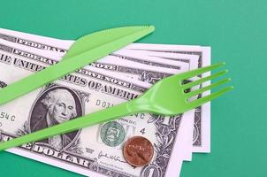 Disposable plastic cutlery green. Plastic fork and knife lie on a small amount of US dollars photo