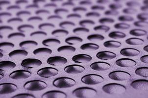 Black metal computer case panel mesh with holes on purple background. Abstract close up photo