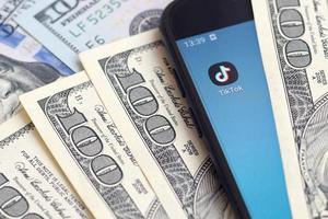 Smartphone screen with Tiktok app and lot of hundred dollar bills. Business and social networking concept photo