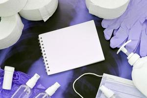 Set of items for Covid-19 quarantine. Empty notepad page and toilet paper, rubber gloves with surgical face mask and hand sanitizer with liquid soap bottle on human chest x-ray film photo