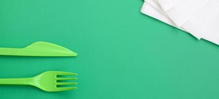 Disposable plastic cutlery green. Plastic fork and knife lie on a green background surface next to napkins photo