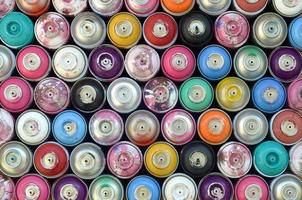 Large number of used colorful spray cans of aerosol paint lying on the treated wooden surface in the artist's graffiti workshop close up. Dirty and stained cans for art photo