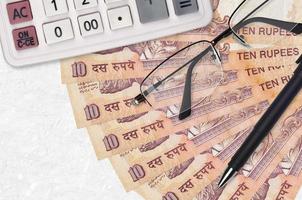 Ventilador de billetes de 10 rupias indias y calculadora con gafas y bolígrafo. préstamo comercial o concepto de temporada de pago de impuestos foto