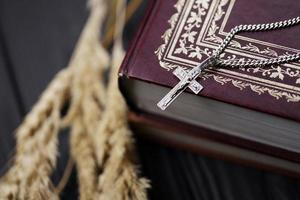 Silver necklace with crucifix cross on christian holy bible book on black wooden table. Asking blessings from God with the power of holiness photo