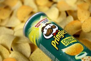 Pringles cheese onion flavour. Cardboard tube can on many Pringles potato chips background. Pringles is a brand of potato snack chips owned by Kellogg Company photo