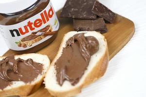 kharkov, ucrania - 27 de diciembre de 2020 lata de vidrio de nutella y untada en pan recién horneado. nutella es fabricada por la empresa italiana ferrero introducida por primera vez en 1964 foto