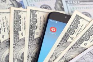 Smartphone screen with Pinterest app and lot of hundred dollar bills. Business and social networking concept photo
