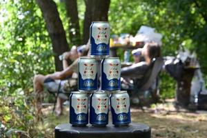 Logotipo de 1664 blanc en latas de cerveza en gran pila con pescadores en el fondo. 1664 blanc es la cerveza de trigo de la cervecería francesa kronenbourg exportada a todo el mundo foto