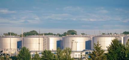 vista de tanques de almacenamiento de combustible, planta de refinería de petróleo a la luz del día contra árboles verdes de verano y cielo azul foto