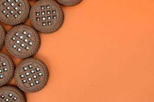 Detailed picture of dark brown round sandwich cookies with coconut filling on an orange surface. Background image of a close-up of several treats for tea photo