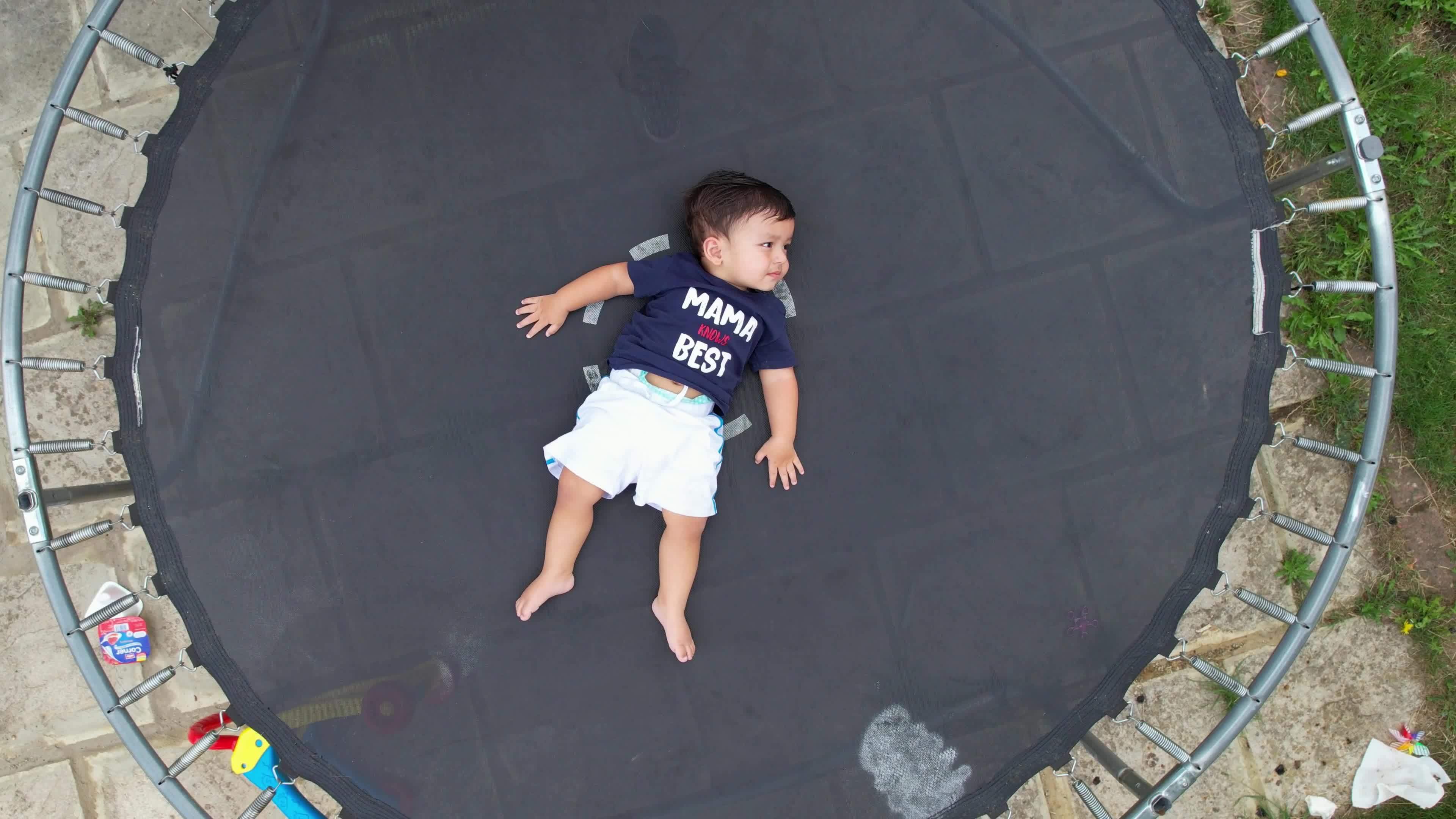 1 Year Old Baby Boy is posing under the drone's camera on a trampoline