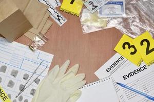 papeleo durante el proceso de investigación de la escena del crimen en el laboratorio csi. etiquetas de evidencia con el solicitante de huellas dactilares y muchos artículos personales confiscados en una mesa de madera foto