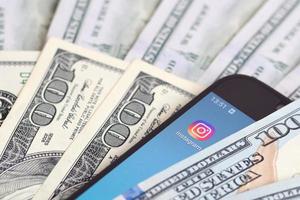 pantalla de teléfono inteligente con aplicación de instagram y muchos billetes de cien dólares. concepto de negocios y redes sociales foto