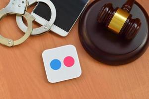 Flickr paper logo lies with wooden judge gavel, smartphone and handcuffs. Entertainment lawsuit concept photo