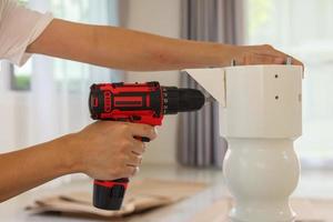 man assembling white table furniture at home using cordless screwdriver photo