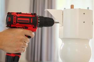 man assembling white table furniture at home using cordless screwdriver photo