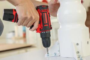 hombre montando muebles de mesa blancos en casa usando un destornillador inalámbrico foto