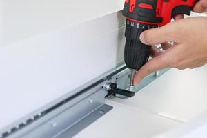 man assembling white table furniture at home using cordless screwdriver photo