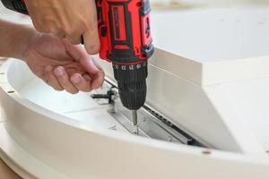 man assembling white table furniture at home using cordless screwdriver photo