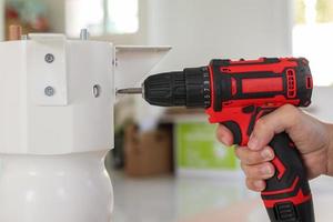 man assembling white table furniture at home using cordless screwdriver photo