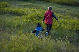 Children in the open spaces of the field are walking among the juicy spring grass in the light of sunset along a narrow trampled path photo