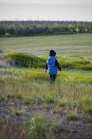 Children in the open spaces of the field are walking among the juicy spring grass in the light of sunset along a narrow trampled path photo