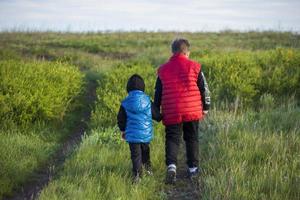 Children in the open spaces of the field are walking among the juicy spring grass in the light of sunset along a narrow trampled path photo