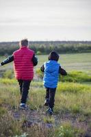 Children in the open spaces of the field are walking among the juicy spring grass in the light of sunset along a narrow trampled path photo