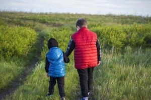 Children in the open spaces of the field are walking among the juicy spring grass in the light of sunset along a narrow trampled path photo