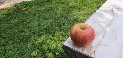 An apple at the end of a marble table on a green grass background photo