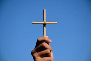 pequeña cruz de madera sosteniendo en la mano con fondo de cielo azul y nublado, concepto de amor, esperanza, verdad, fe, creer en Jesús, enfoque suave y selectivo. foto