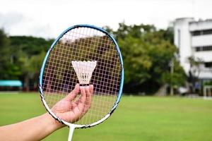 raqueta de bádminton y volantes de bádminton tomados de la mano para jugar al aire libre, enfoque suave y selectivo en cuerdas y raquetas, concepto de actividad al aire libre. foto