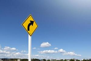 Traffic sign, left arrow curve sign on white pole by the main road with blue sky background, soft and selective focus. photo