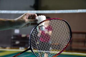 Men single badminton player holds racket and white cream shuttlecock in front of the net before serving it to another side of the court, soft and selective focus. photo