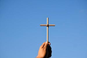 Small wooden cross holding in hand with cloudy and blue sky background, concept for love, hope, truth, faith, believe in Jesus, soft and selective focus. photo