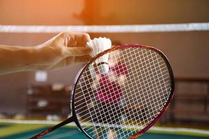 Men single badminton player holds racket and white cream shuttlecock in front of the net before serving it to another side of the court, soft and selective focus. photo