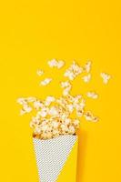 refrigerio de ver el concepto de película, palomitas de maíz dulces flotan desde un vaso de papel sobre fondo amarillo