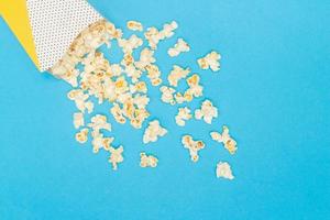 refrigerio de ver el concepto de película, palomitas de maíz dulces derramadas de un vaso de papel sobre fondo azul claro foto
