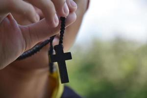 Asian young Christian boy shows his wooden rosary necklace with a cross, soft and selective focus, concept for showing pride in being a Christian to other people around the world.