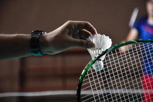Men single badminton player holds racket and white cream shuttlecock in front of the net before serving it to another side of the court, soft and selective focus. photo