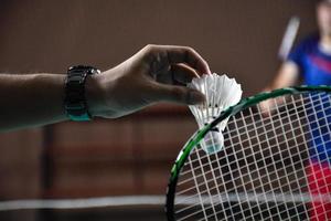 Men single badminton player holds racket and white cream shuttlecock in front of the net before serving it to another side of the court, soft and selective focus. photo