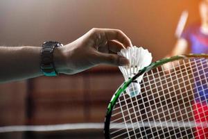 Men single badminton player holds racket and white cream shuttlecock in front of the net before serving it to another side of the court, soft and selective focus. photo