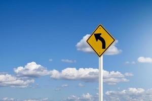 Traffic sign, left arrow curve sign on white pole by the main road with blue sky background,soft and selective focus. photo