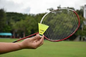 raqueta de bádminton y volantes de bádminton tomados de la mano para jugar al aire libre, enfoque suave y selectivo en cuerdas y raquetas, concepto de actividad al aire libre. foto