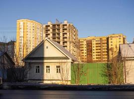 Urbanization. Old small houses against the background of large high-rise buildings photo