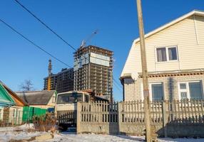 high-rise construction.  Old small houses against the background of large high-rise buildings photo