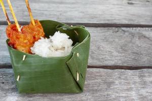 Grilled pork with sticky rice in natural made container to reduce the use of plastic on wooden table. photo