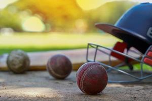 Cricket sports equipment including Cricket Balls, cricket bat , cricket helmet On the cement floor, focus on the red  Balls at the very front. photo