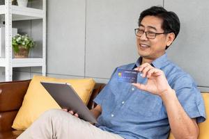 Selective focus at credit card. Senior Asian men hand holding credit card and fill in payment information for online shopping. Wireless internet technology with elderly concept. photo