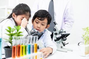 Young Asian boy and girl student wearing protective google while study and do science experiment in classroom with teacher. Learning and having fun moment. Chemist or biology classroom concept. photo